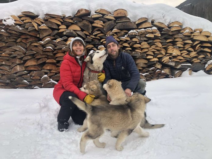 Un couple et un jeune chiot devant une corde de bois.